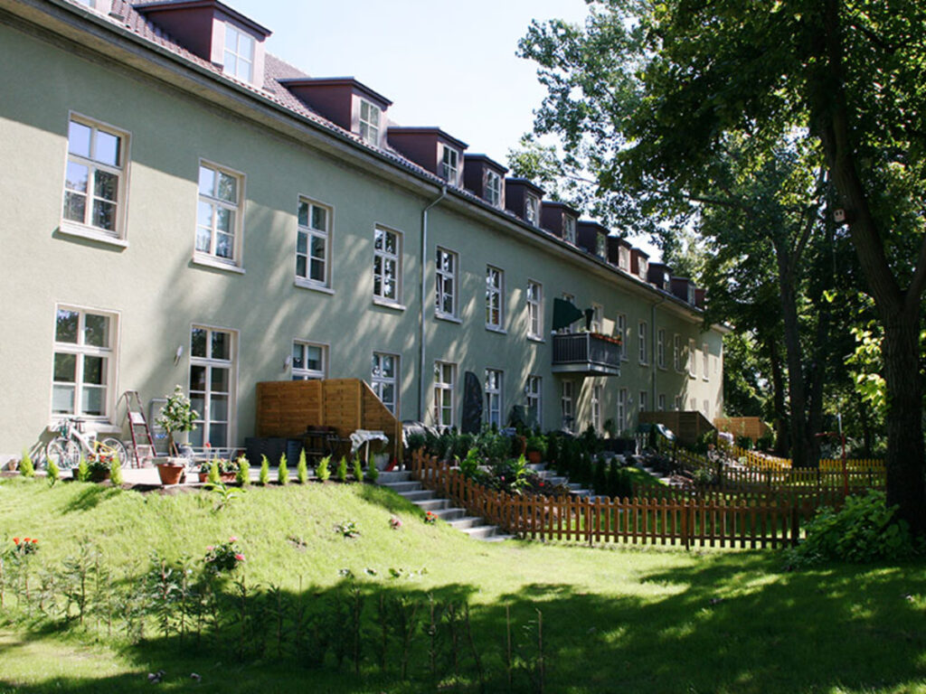 Reihenhaus mit Garten, Holzzaun und Bäumen im Sommer.