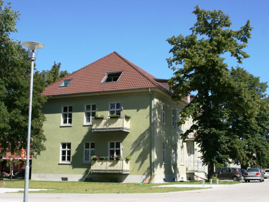 Grünes Wohnhaus mit rotem Dach und Bäumen.