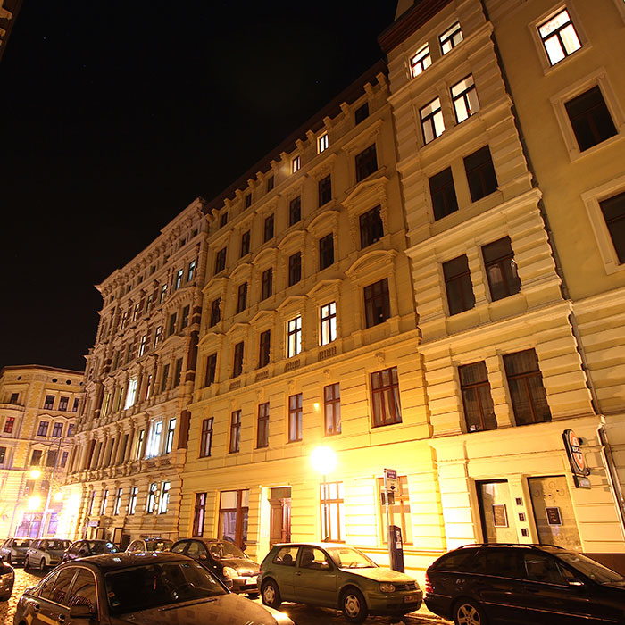 Nachts beleuchtete Altbau-Fassade mit parkenden Autos.