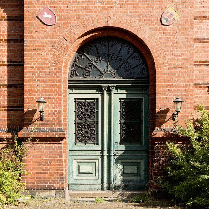 Grüne Holztür in roter Backsteinfassade mit Wappen.