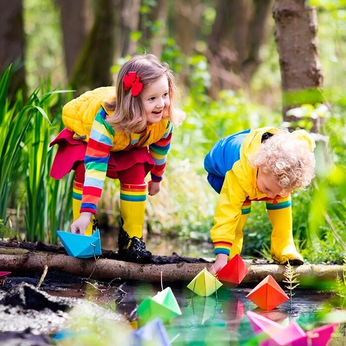 Kinder spielen mit Papierbooten am Bach im Wald.