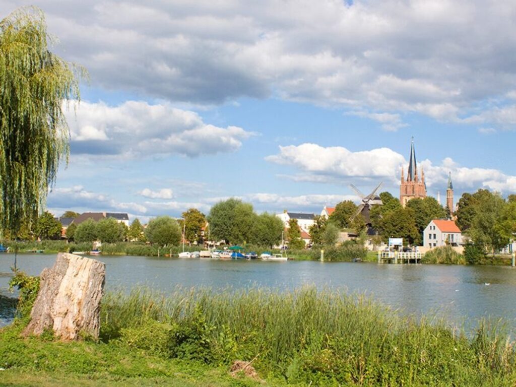 See mit Bäumen, Kirche und Wolken im Hintergrund.